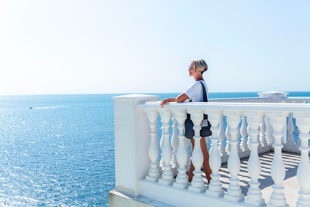 Una donna su una bella passeggiata con ringhiere bianche guarda il mare in una giornata di sole Viaggi turistici e attività ricreative