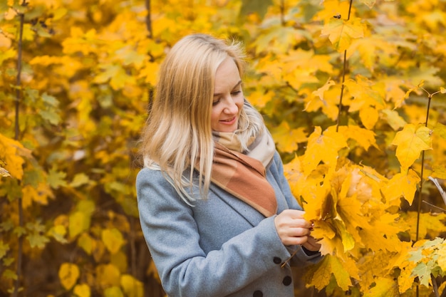 Una donna tiene in mano foglie di acero giallo in un parco su uno sfondo di alberi