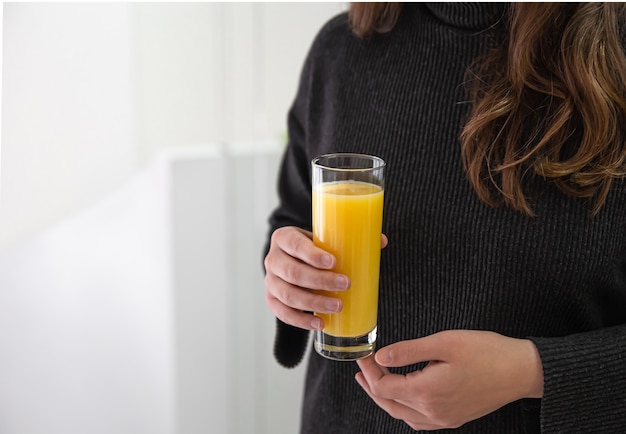 Una donna tiene in mano un bicchiere di succo d'arancia appena spremuto, primo piano.