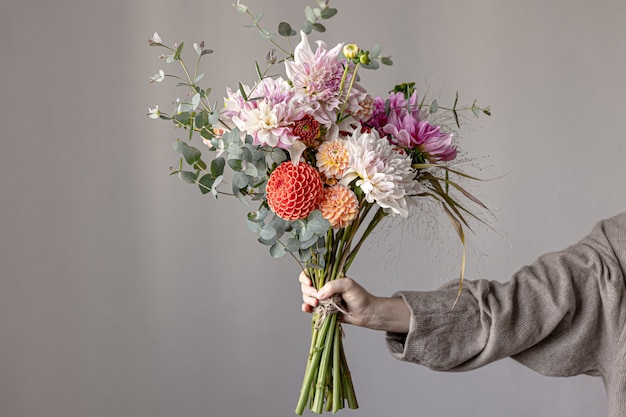 Una donna tiene in mano una composizione floreale festiva con fiori di crisantemo luminosi, un bouquet festivo.