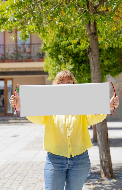 Una donna tiene un cartello vuoto davanti al suo viso Mockup