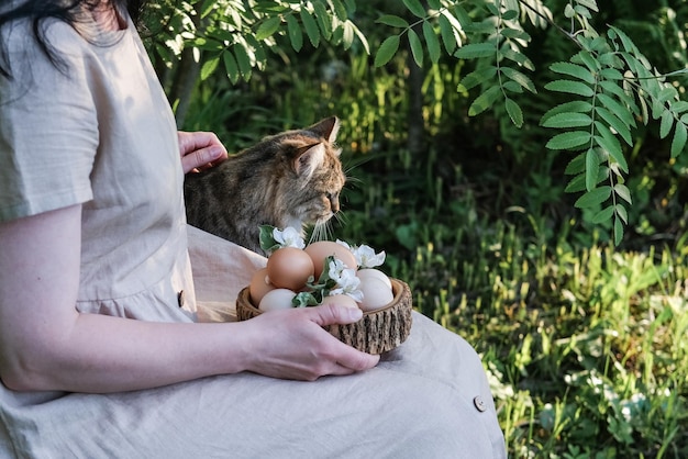 Una donna tiene un piatto di legno con uova di Pasqua e accarezza un gatto Pasqua in stile rustico