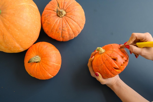 Una donna tiene una piccola zucca e ritaglia una smorfia malvagia su di essa con un tagliacarte su uno sfondo nero Vista dall'alto del concetto di Halloween