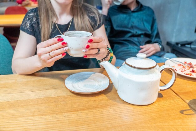 Una donna tiene una tazza di tè e una teiera su un tavolo.