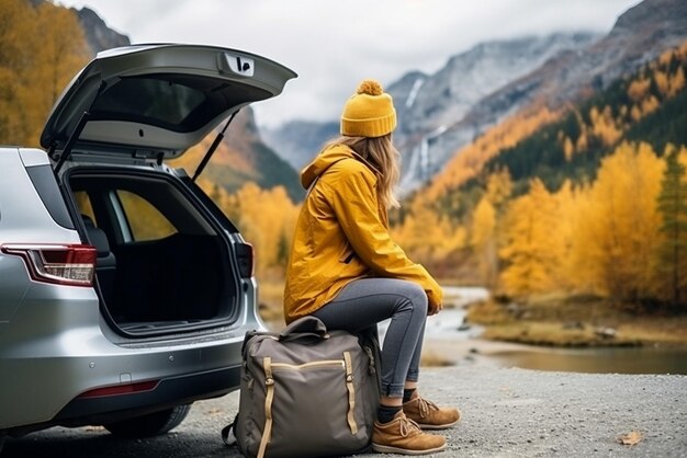 una donna turistica con uno zaino si siede sul bagagliaio di un'auto nelle montagne