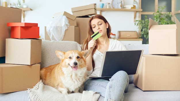 Una donna usa un computer portatile per fare acquisti online a casa. Conferma d'acquisto via Internet. Rilegare una carta per lo shopping online. Una donna seduta sul divano con un cane carino mentre fa shopping online.