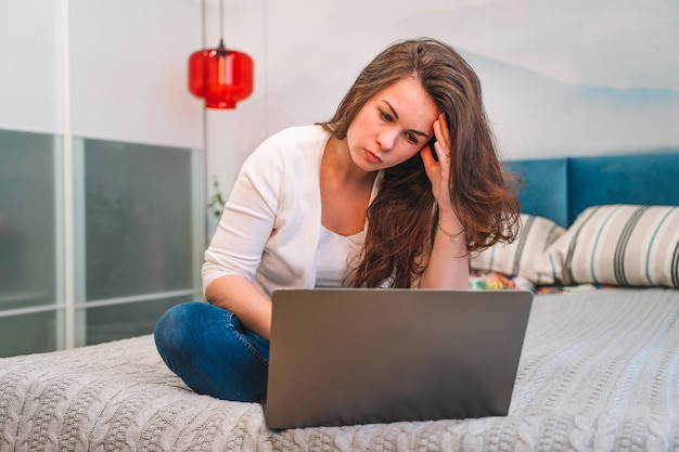 Una donna usa un laptop mentre è sdraiata sul letto. Concetto di home office e formazione online.