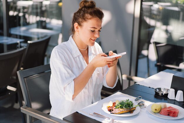 Una donna usa un telefono e mangia il pranzo o la colazione all'aperto in un caffè