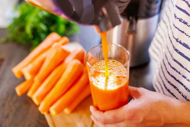 Una donna versa del succo di carota fresco in un bicchiere di succo di carrota appena spremuto