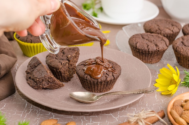 Una donna versa il cioccolato fuso sui muffin al cioccolato. Messa a fuoco selettiva. Dolci fatti in casa