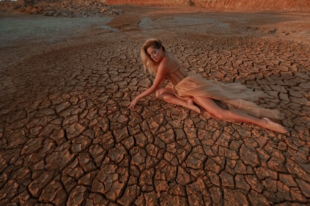 Una donna vestita con un abito lungo siede nel deserto sul terreno incrinato