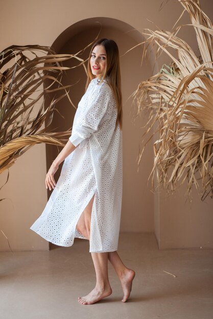 Una donna vestita di bianco si trova di fronte a un muro con delle piante.