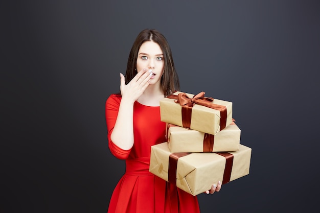 Una donna vestita di rosso ha aperto la bocca sorpresa, tenendo in mano palloncini e confezioni regalo