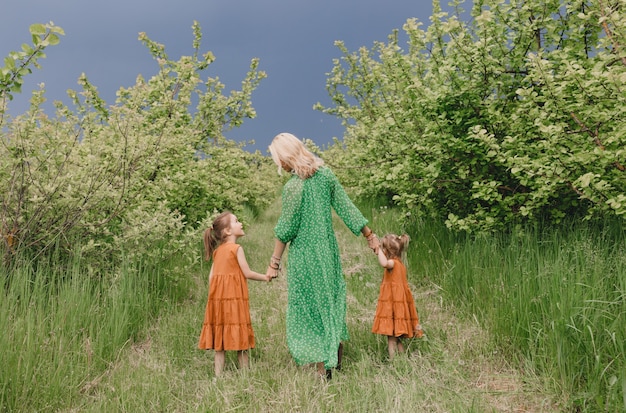 Una donna vestita di verde cammina con due bambine in un meleto primaverile.