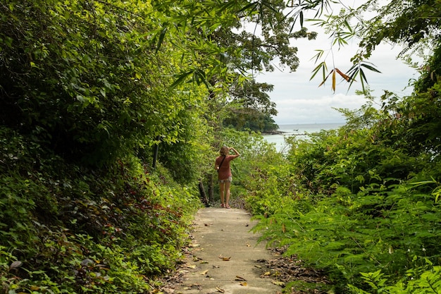 Una donna viaggiatrice alla fine di un sentiero circondato dalla foresta tropicale che guarda verso la spiaggia