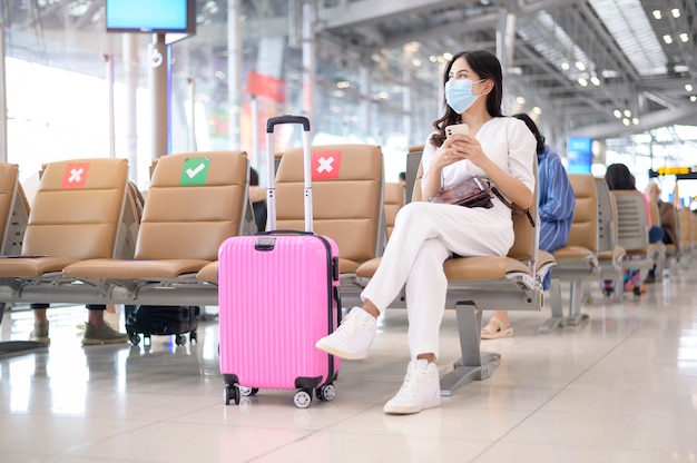 Una donna viaggiatrice indossa una maschera protettiva in aeroporto internazionale, viaggia sotto la pandemia Covid-19,