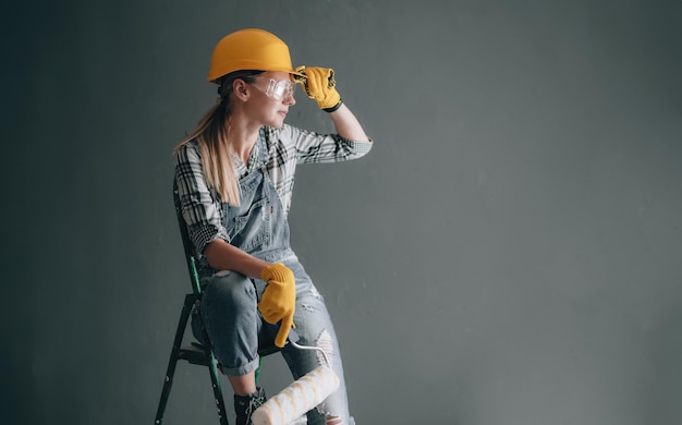 Una donna volitiva in un casco da costruzione guanti occhiali e tute è impegnata in lavori di riparazione e costruzione a casa concetto di una donna forte e indipendente