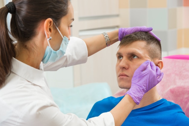 Una dottoressa allunga la pelle sul viso di un paziente maschio controllando l'elasticità della pelle prima della procedura di ringiovanimento nella clinica cosmetica