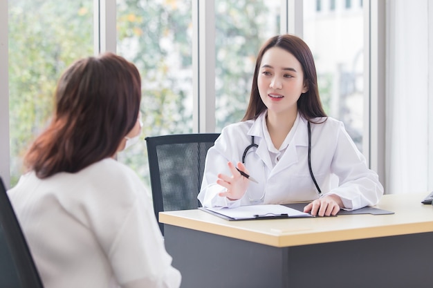 Una dottoressa asiatica professionista che indossa un camice medico parla con una paziente