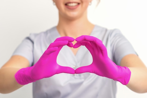 Una dottoressa caucasica sorridente che indossa guanti rosa in uniforme che mostra il simbolo di un cuore su uno sfondo bianco.