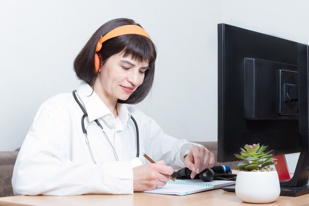 Una dottoressa che indossa un auricolare effettua una videochiamata online con un paziente, firma un documento nel suo ufficio