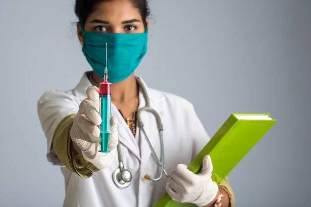 Una dottoressa con uno stetoscopio tiene e mostra un'iniezione o una siringa con referto medico o libro.