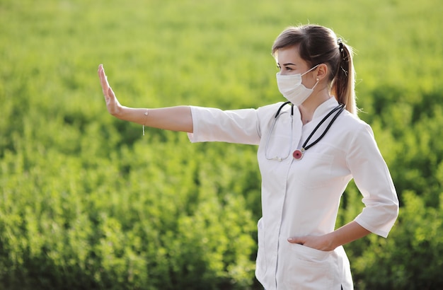 Una dottoressa in una maschera medica che mostra una fermata su sfondo verde erba