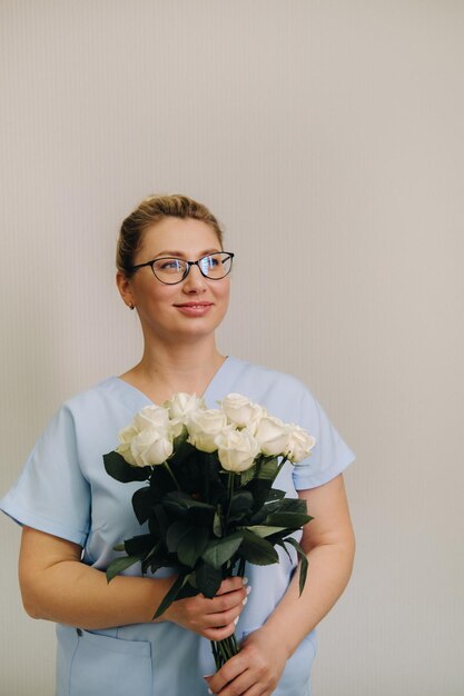 Una dottoressa in una veste blu con un mazzo di rose bianche tra le mani