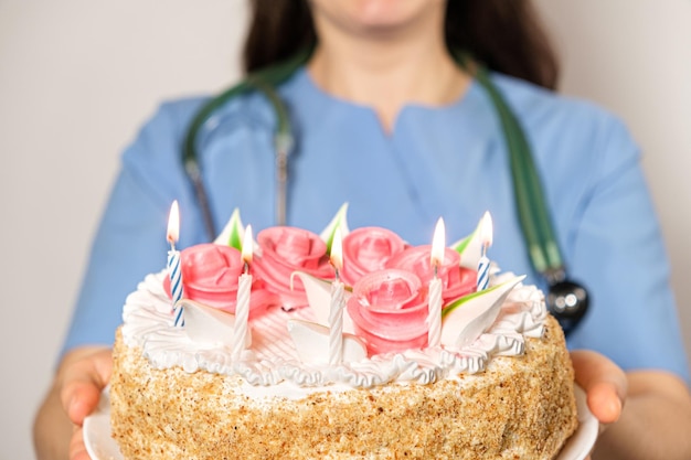 Una dottoressa in uniforme blu tiene una torta di compleanno con le candele