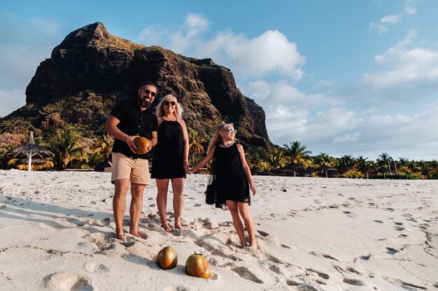 Una famiglia alla moda in abiti neri con noci di cocco in mano sulla spiaggia dell'isola di Mauritius.Bella famiglia sull'isola di Mauritius nell'Oceano Indiano.