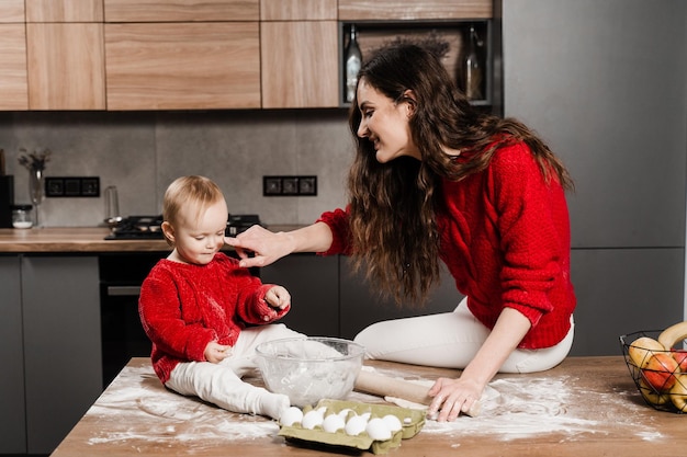 Una famiglia amorevole e felice sta cucinando insieme cibo da forno fatto in casa Madre e piccola figlia aiutante stanno preparando i biscotti e si divertono in cucina a casa