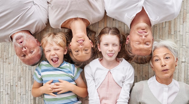 Una famiglia che si lega insieme ed è giocosa mostrando espressioni diverse mentre si lega e si gode del tempo di qualità Al di sopra di una famiglia felice e divertente che fa facce sciocche sdraiate insieme su un pavimento di casa a casa