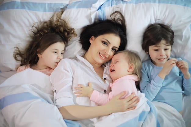 Una famiglia con bambini che si diverte sul letto sotto le coperte durante le vacanze di Natale