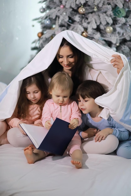 Una famiglia con bambini che si divertono sul letto sotto le coperte durante le vacanze di Natale.