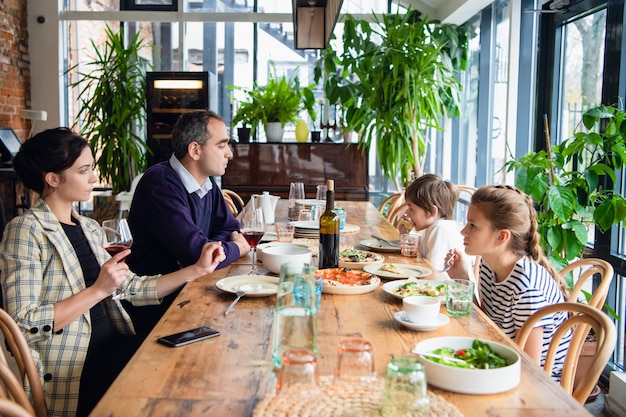 Una famiglia con bambini in un bar, i genitori bevono vino.