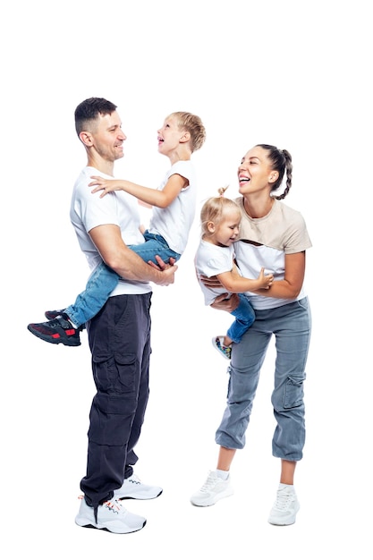 Una famiglia con due bambini piccoli che ridono e si abbracciano. Mamma, papà, figlio e figlia con magliette e pantaloni bianchi. Amore e tenerezza. Isolati su uno sfondo bianco. Verticale.