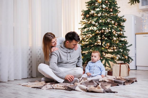 Una famiglia con un figlio piccolo si siede vicino a un albero di Natale e dà il benvenuto al nuovo anno