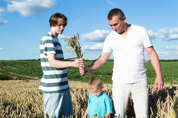Una famiglia con un papà, un adolescente e un bambino piccolo camminano spensierati e divertenti in un campo di grano È tempo di raccogliere La crisi alimentare nel mondo