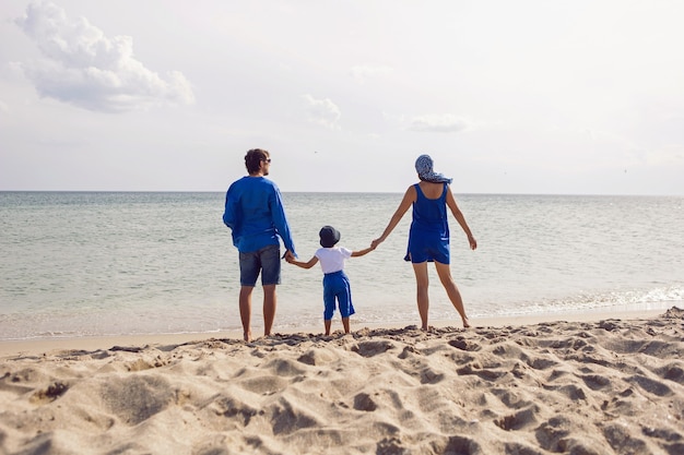 Una famiglia di tre persone in abiti blu si trova su una spiaggia sabbiosa il mare in estate in vacanza