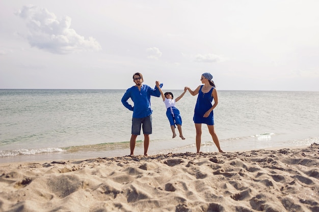Una famiglia di tre persone in abiti blu si trova su una spiaggia sabbiosa in riva al mare in estate in vacanza