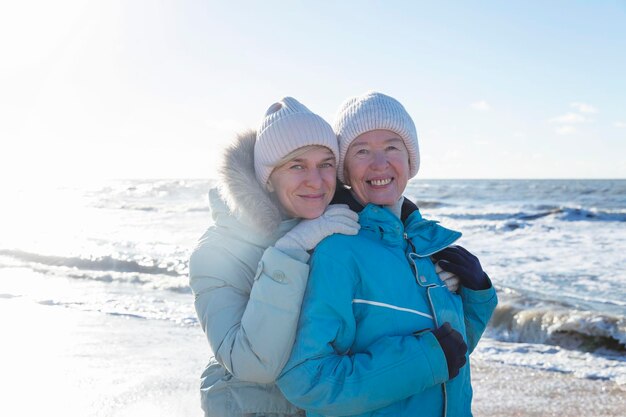 Una famiglia felice cammina lungo la spiaggia sabbiosa in inverno ridendo donne giovani e vecchie abbracciando amore e tenerezza