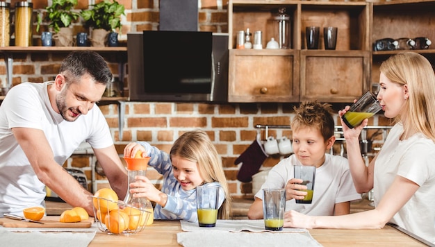 Una famiglia felice di quattro persone prepara il succo d'arancia per colazione in cucina