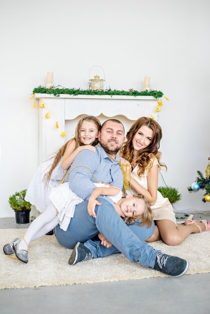 Una famiglia felice è seduta sul tappeto accanto al caminetto bianco con un elegante albero di Natale