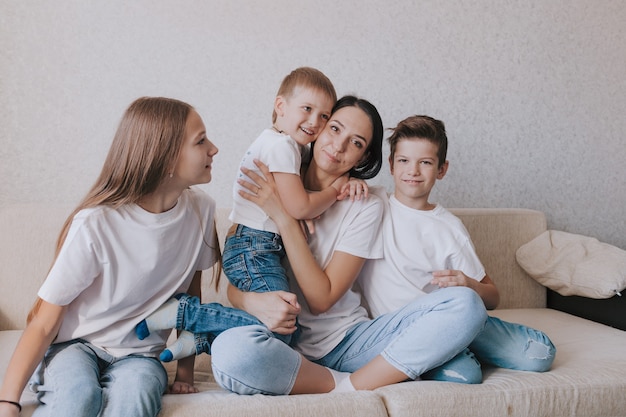 Una famiglia felice in jeans e magliette bianche è seduta sul divano. La mamma abbraccia un bambino piccolo.