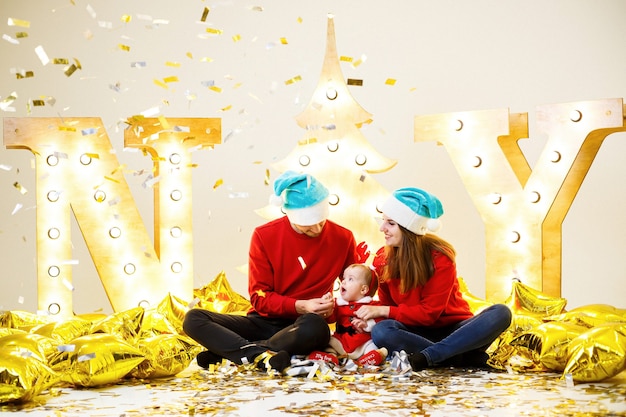 Una famiglia felice in maglioni rossi è seduta insieme sul pavimento. Atmosfera natalizia. Un bambino in costume da Babbo Natale. Concetto di relazione familiare