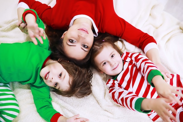 Una famiglia in pigiama a righe riposa a casa. I bambini vestiti da elfi sono sdraiati sul divano. Una famiglia felice.