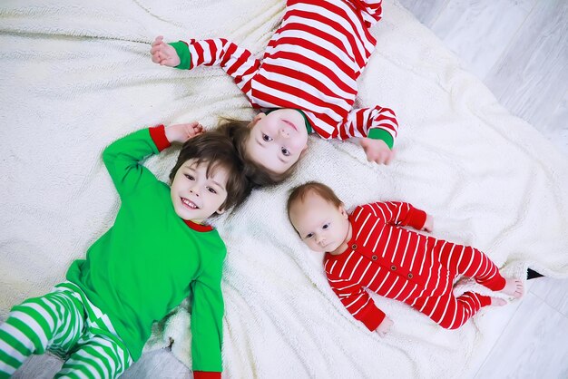 Una famiglia in pigiama a righe riposa a casa. I bambini vestiti da elfi sono sdraiati sul divano. Una famiglia felice.