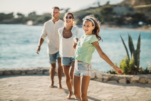 Una famiglia sorridente con un'adolescente che cammina vicino al mare divertendosi alle vacanze estive.