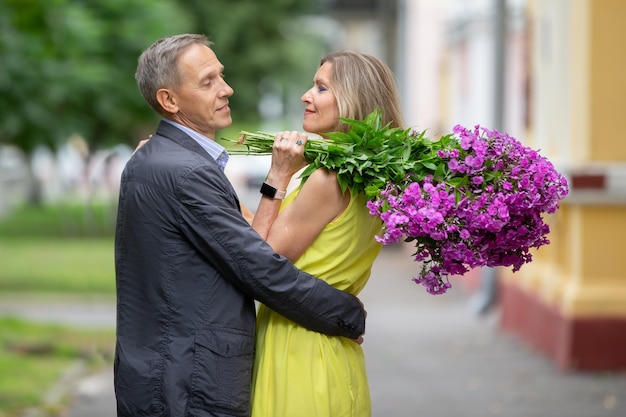 Una felice coppia di anziani con un bouquet di fiori cammina per la città estiva
