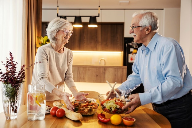 Una felice coppia di anziani sta mettendo un delizioso pranzo su una tavola a casa